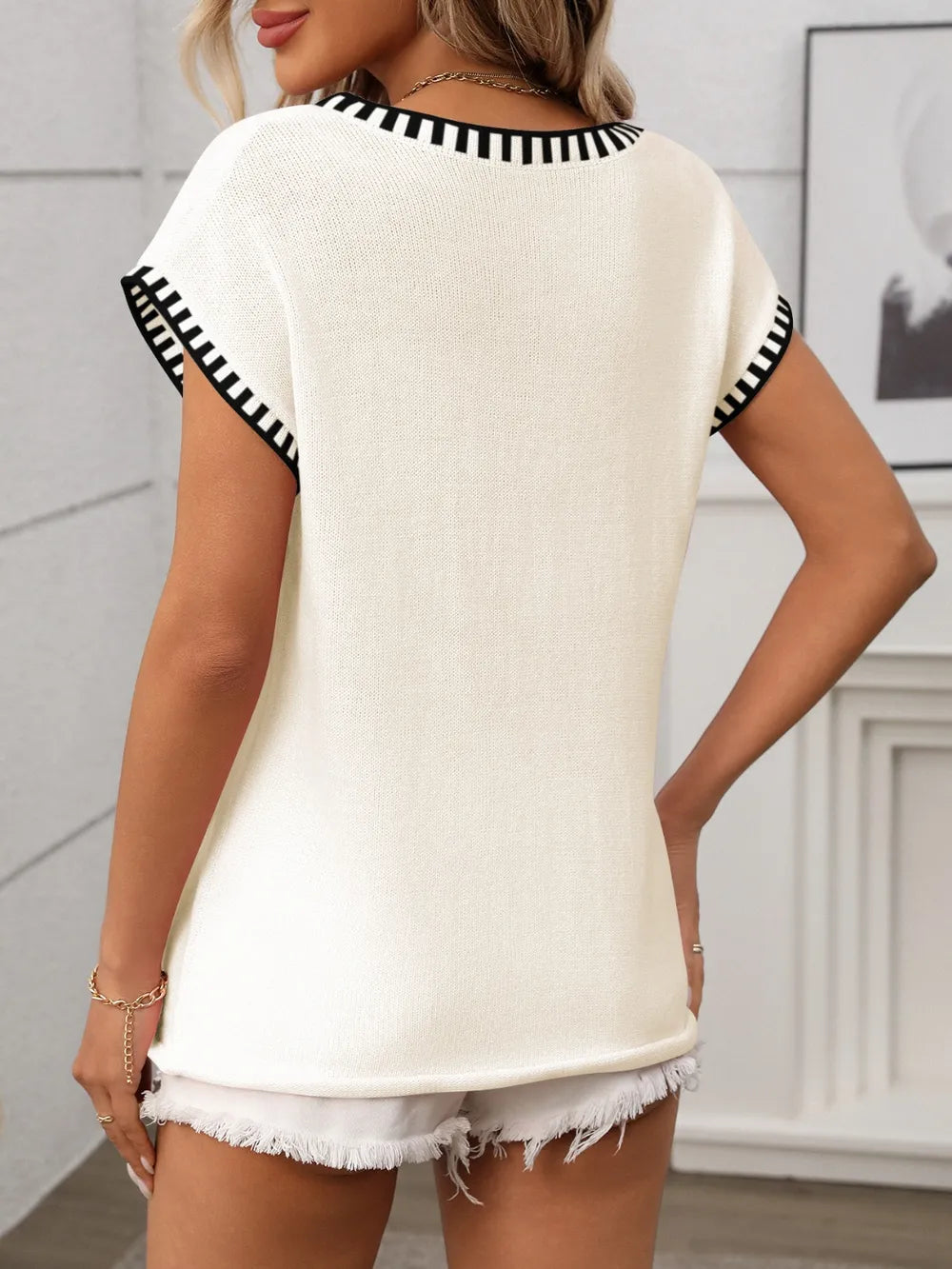Cream knit short-sleeve top with black contrast trim at neckline and sleeves