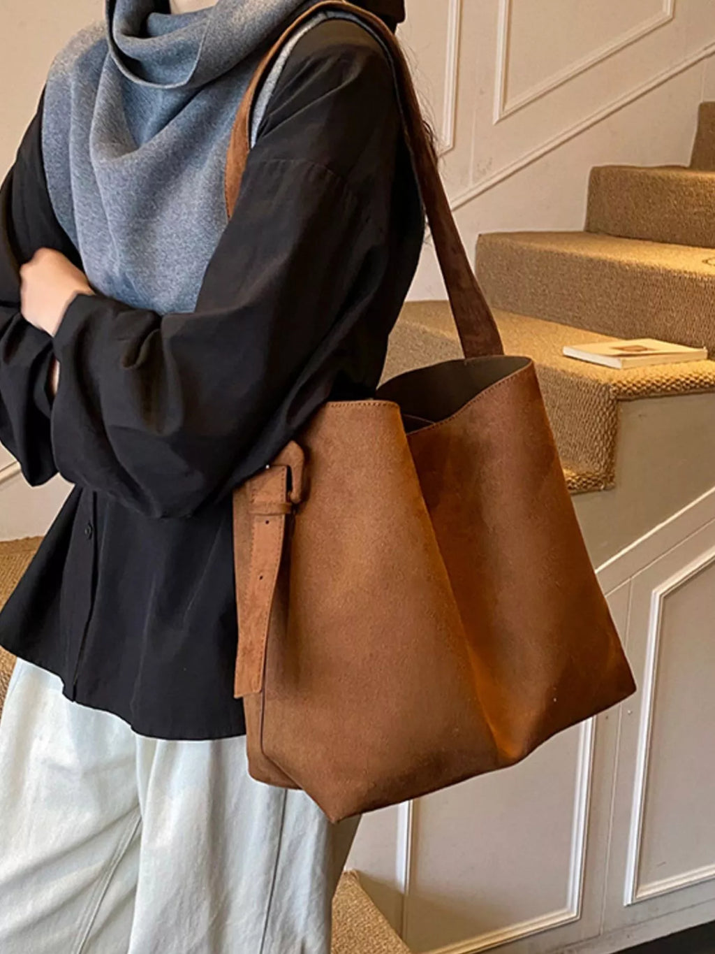 Brown adjustable strap tote bag held by model; slouchy silhouette, open top