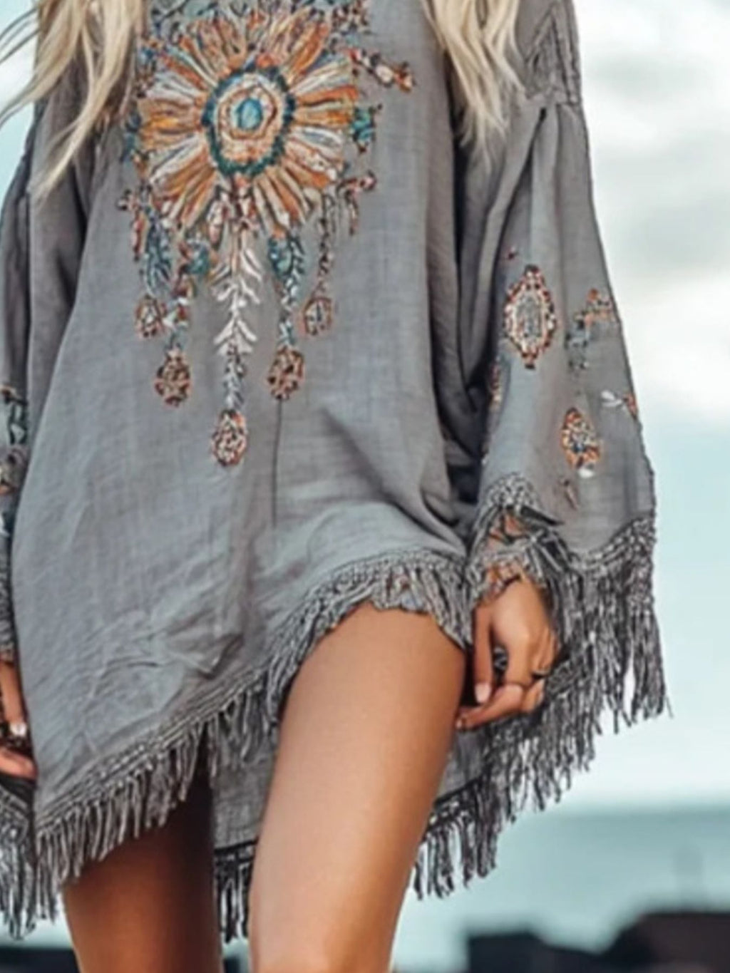 Close-up: grey mini dress with fringe trim hem and colorful floral medallion embroidery