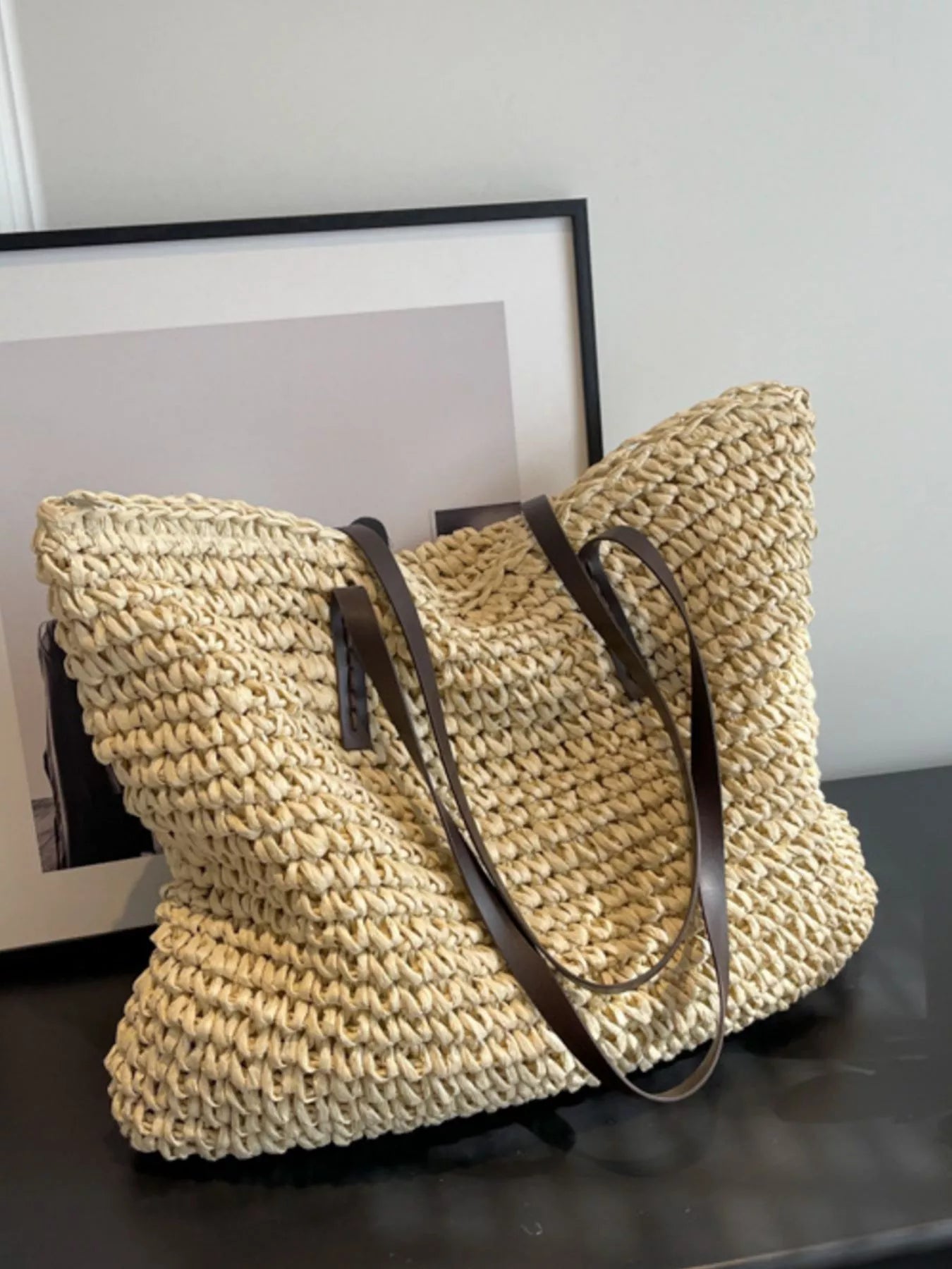Woven straw shoulder bag with black crossbody strap, woven basket tote in light tan, side view