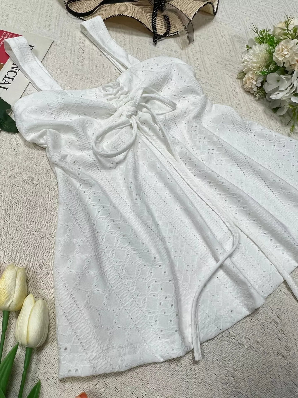 White embroidered cami top laid flat with long drawstrings and eyelet pattern