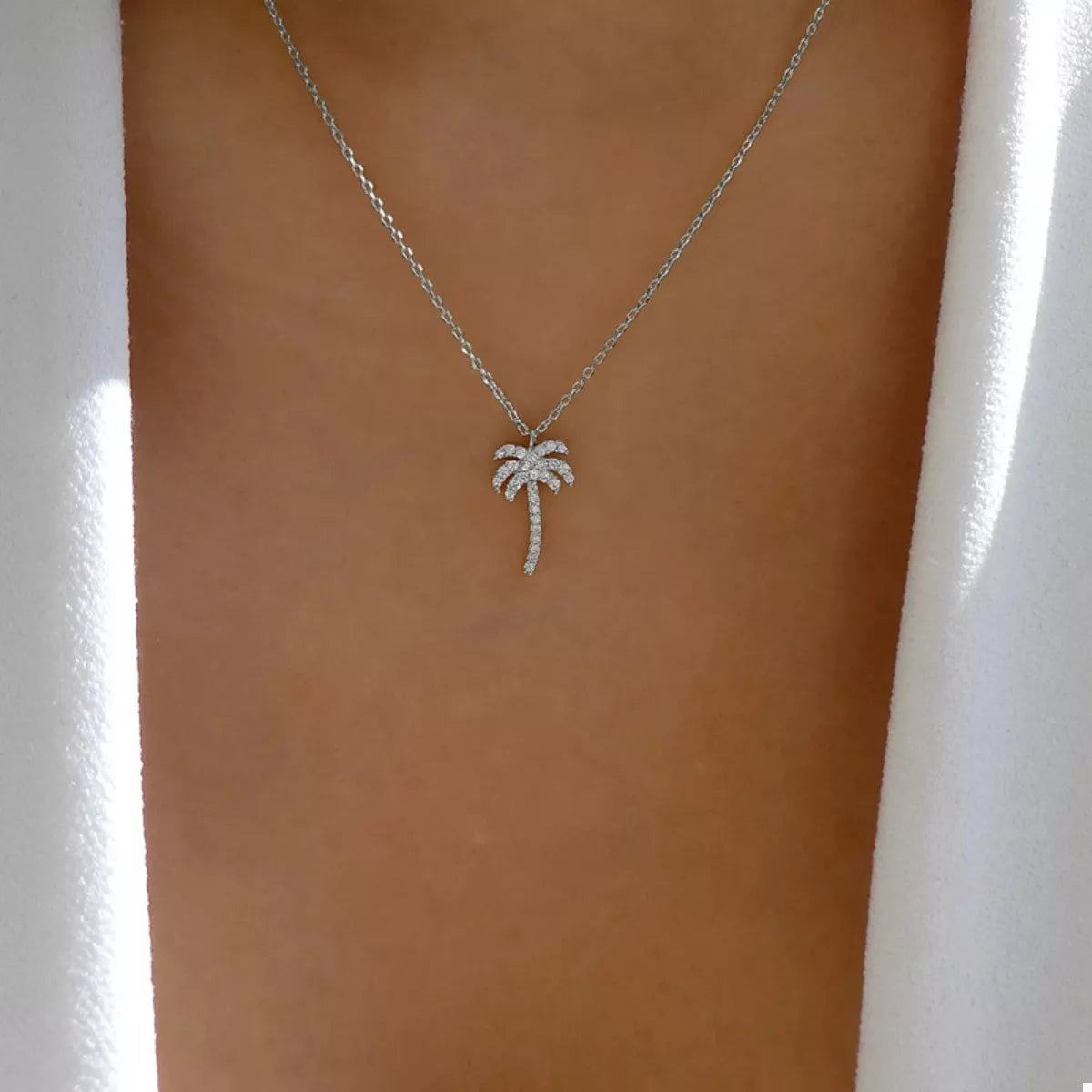 Silver palm tree pendant necklace on a fine chain, centered on the bust