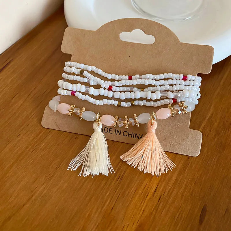 White and pink beaded tassel bracelet with cream tassels and gold-tone charm accents