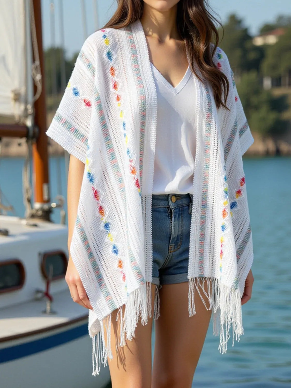 White open-front knit cape with openwork texture and colorful pom-pom pattern, fringe hem