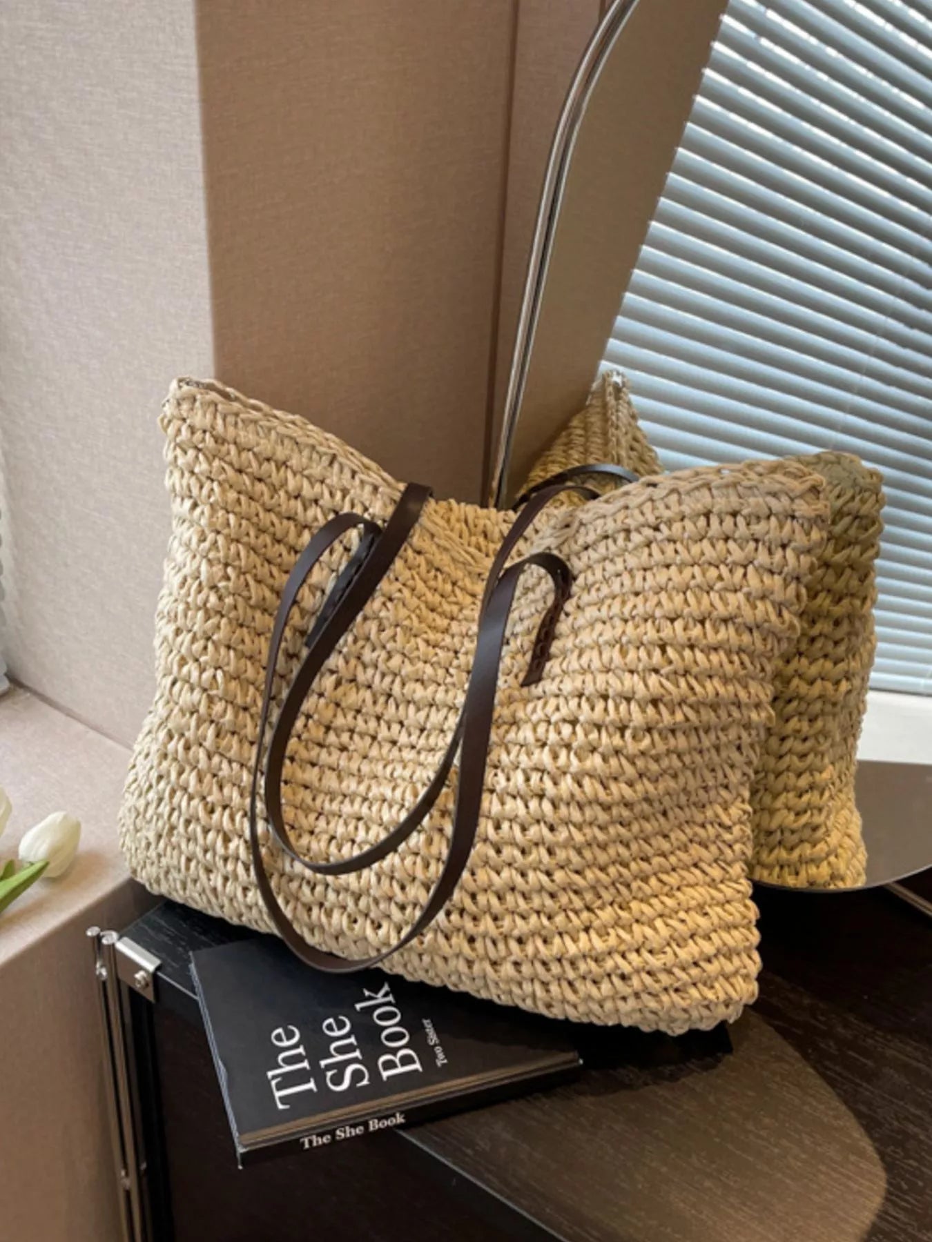 Woven straw shoulder bag with black leather straps, open-top basket style in light khaki