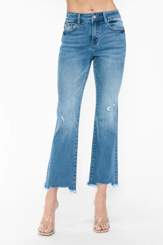 Front close-up of medium-wash mid-rise jeans with five pockets and raw frayed hem