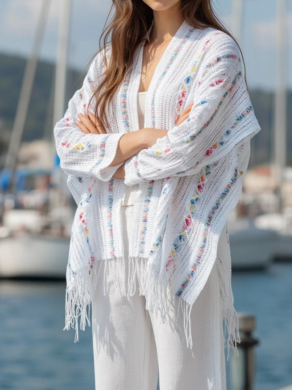 White open-front knit cape with colorful dot accents and fringe, shown from front
