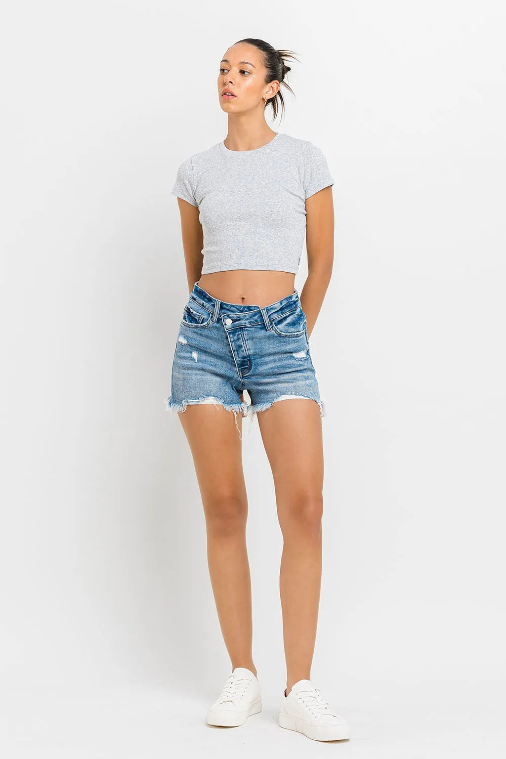 Medium-wash raw-hem denim shorts with frayed edges and stepped waistband, front