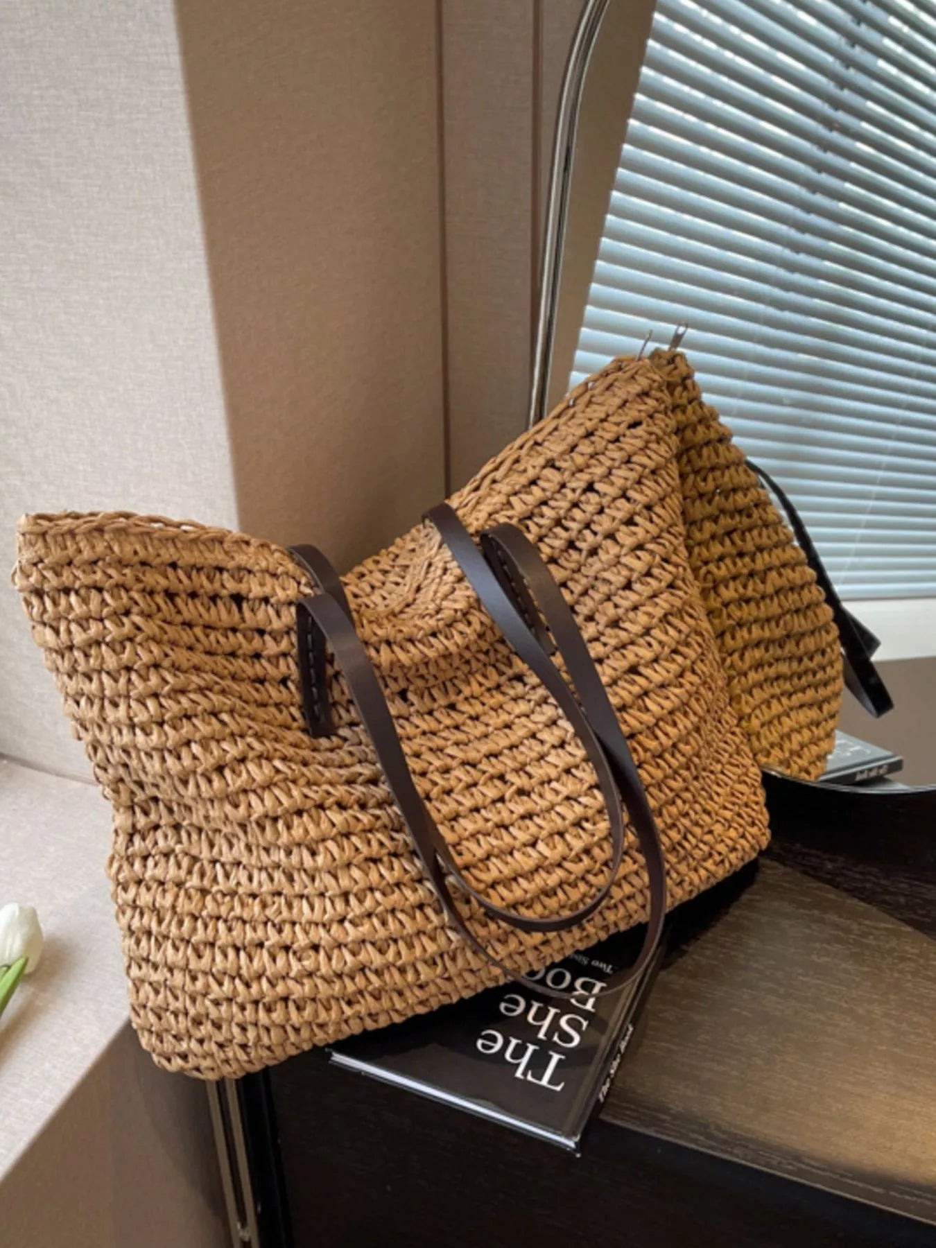 Woven straw shoulder bag with black straps, open basket tote in warm brown/tan straw