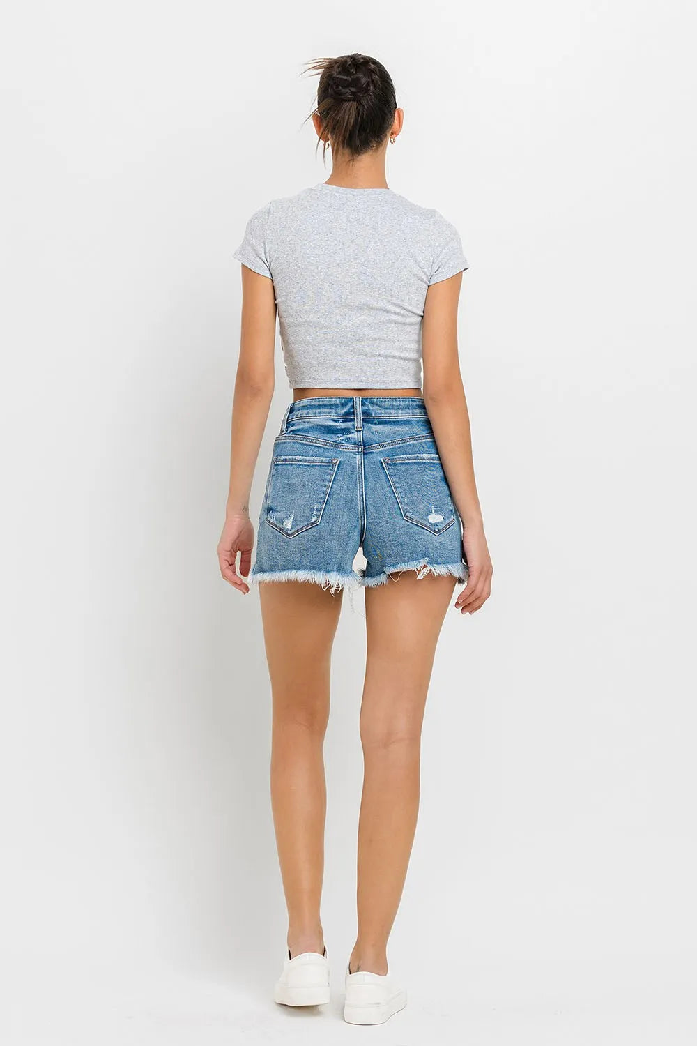 Medium-wash denim shorts, rear view with stepped waistband and frayed raw hem