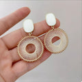 Gold-plated circle dangle earrings with white oval tops and woven ring with center hole