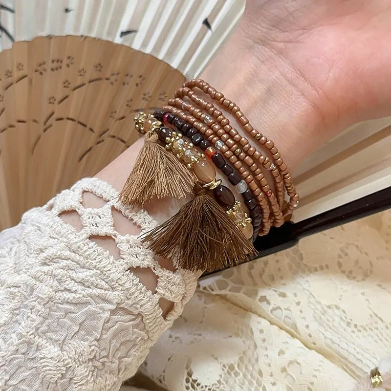 Brown and dark bead tassel bracelet with two tassels and gold-tone charm details