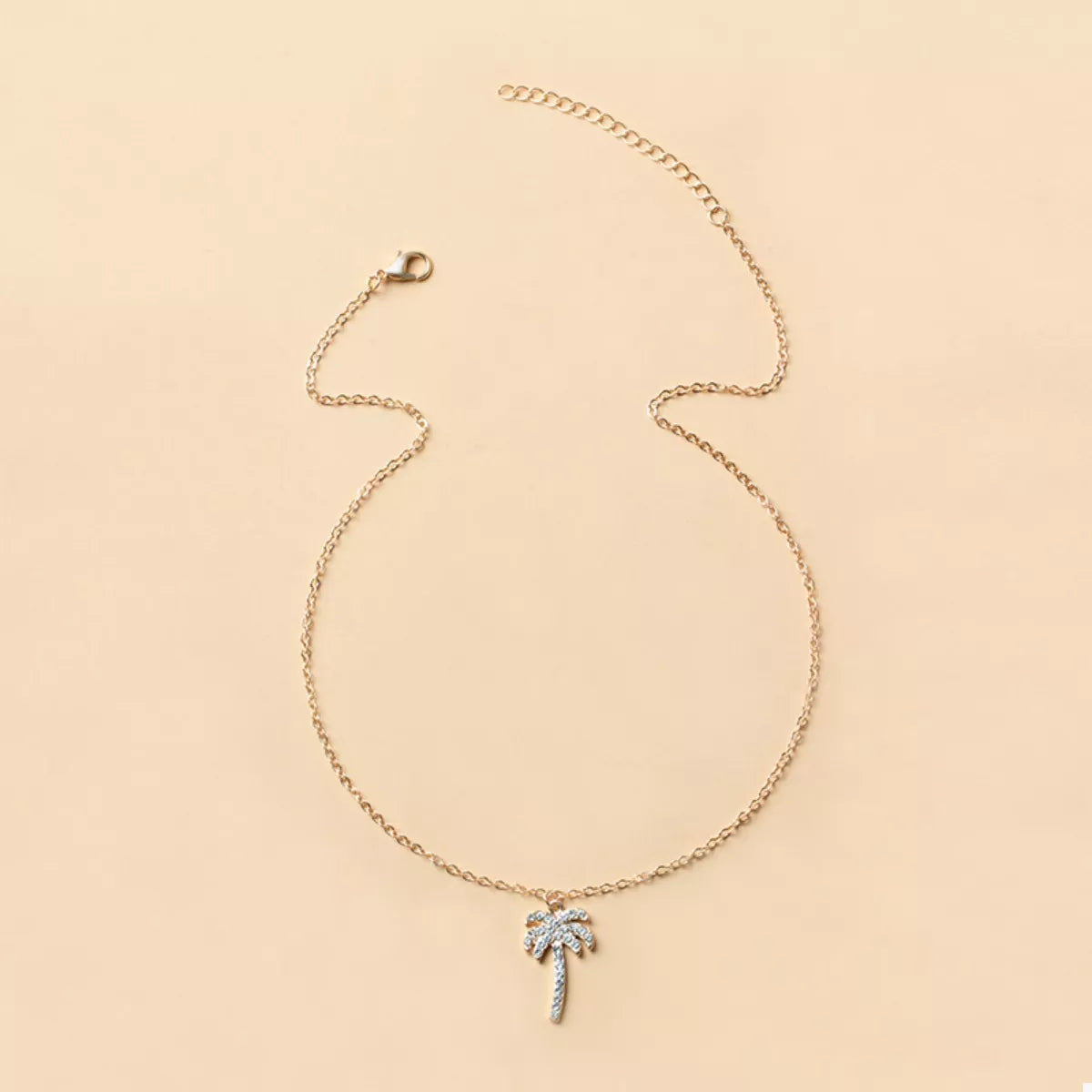Gold palm tree pendant on a delicate chain necklace, lobster clasp visible