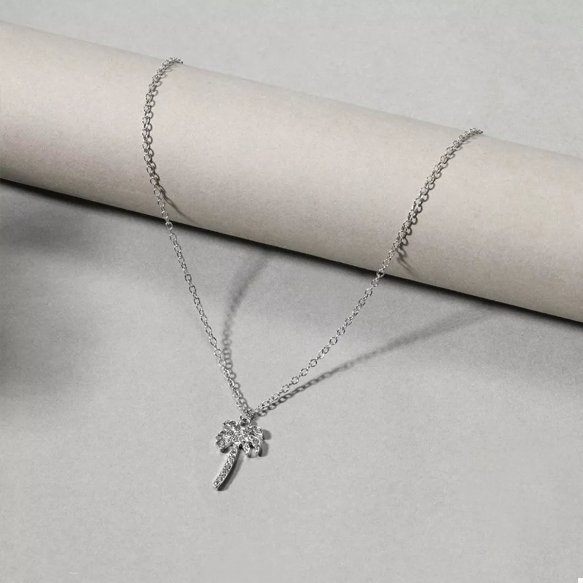 Silver palm tree pendant necklace shown on a cushion, fine chain and pendant