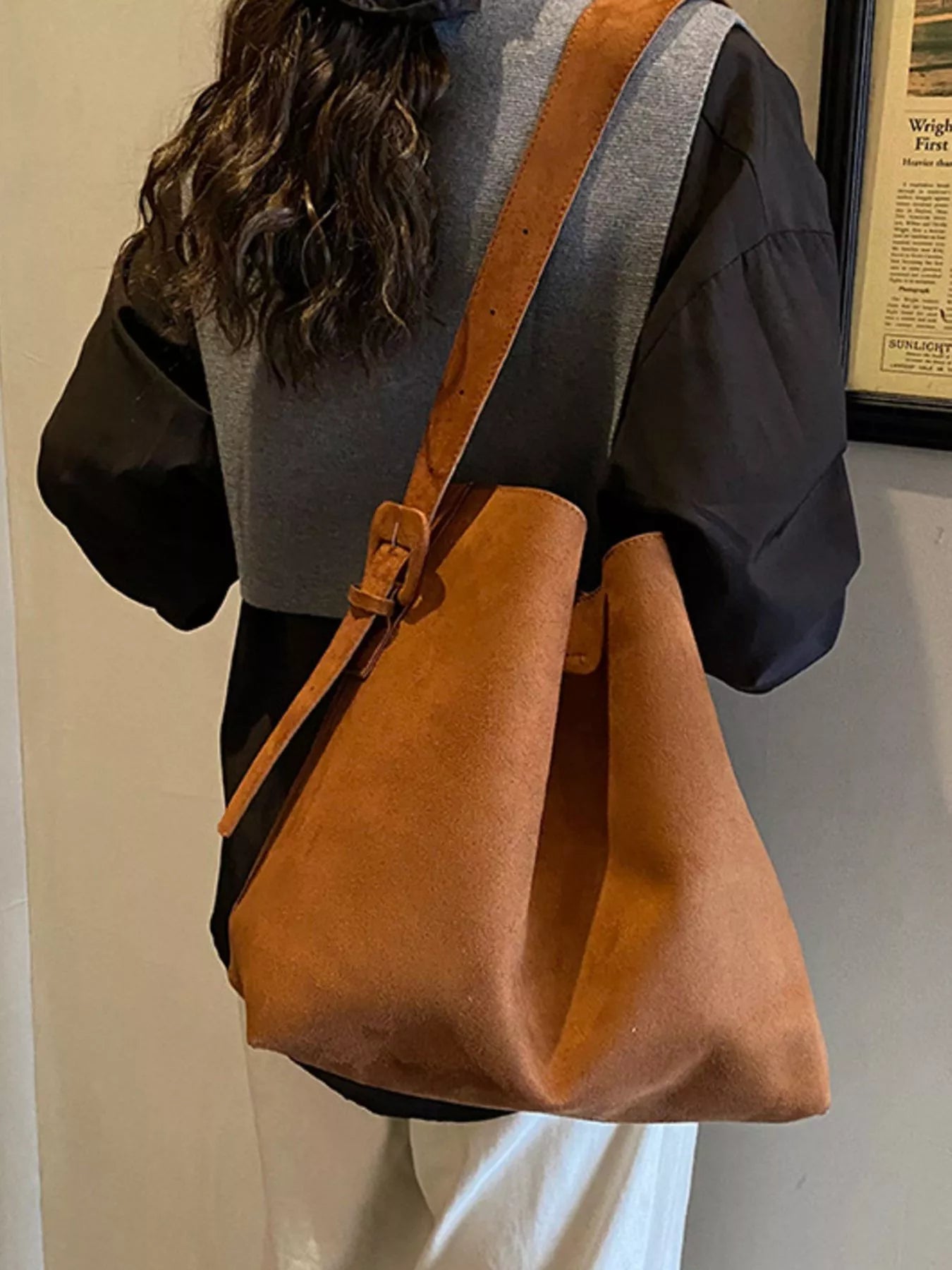 Brown tote bag with long adjustable strap and buckle, held on shoulder