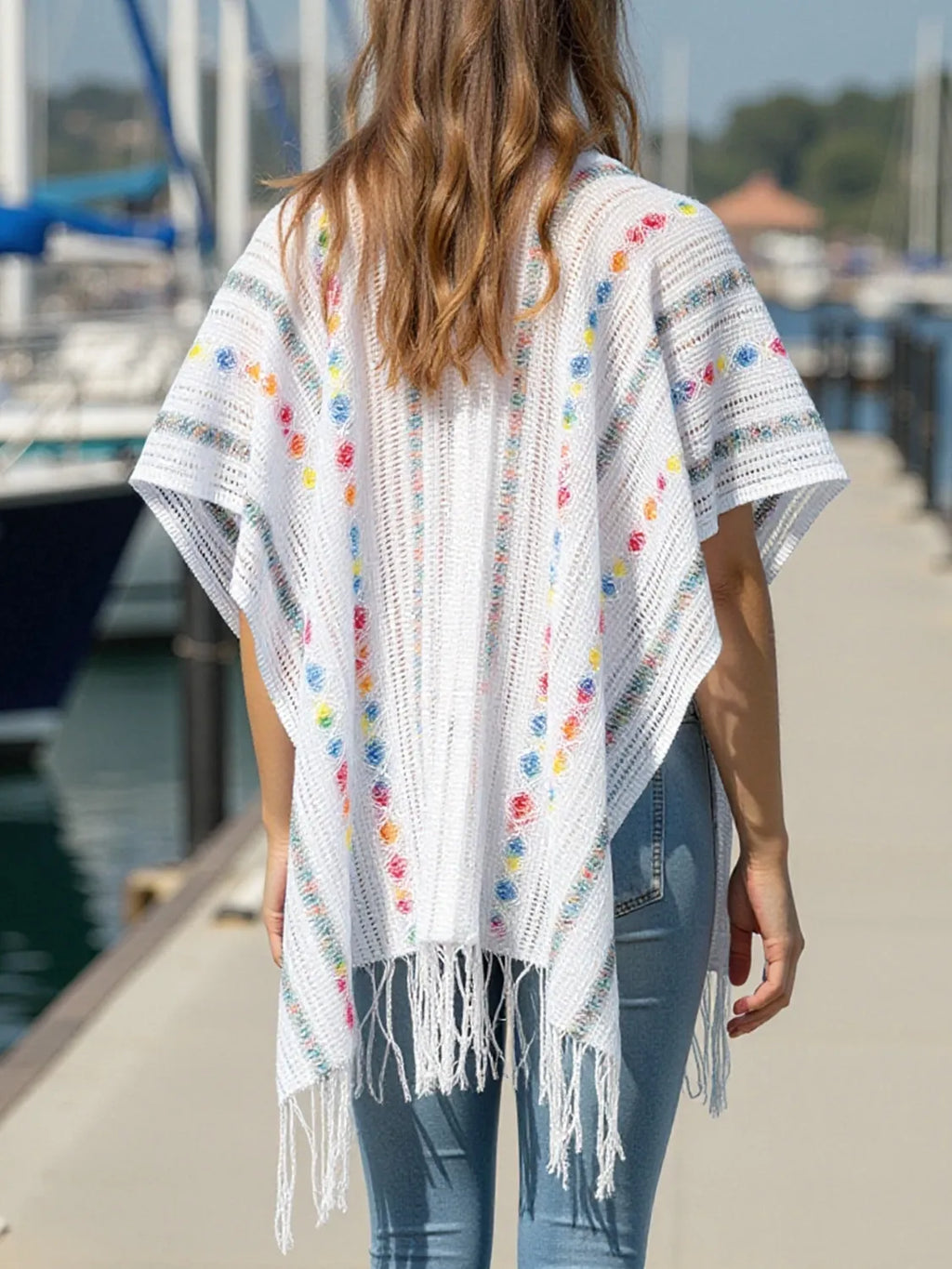 White open-front knit cape with colorful dot trim and long fringe hem, back view