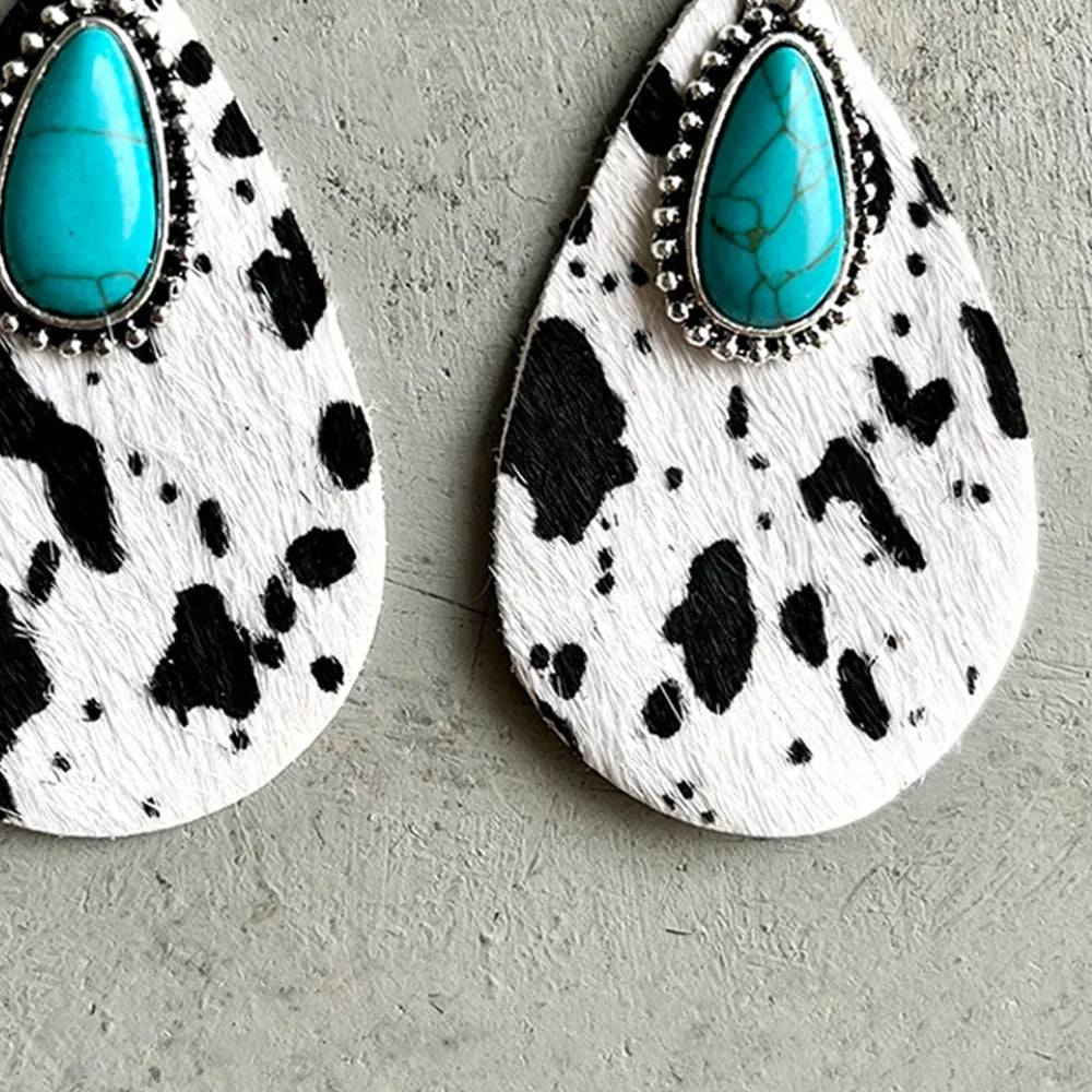 Close-up of turquoise teardrop earrings with cow print leather texture and silver bezel