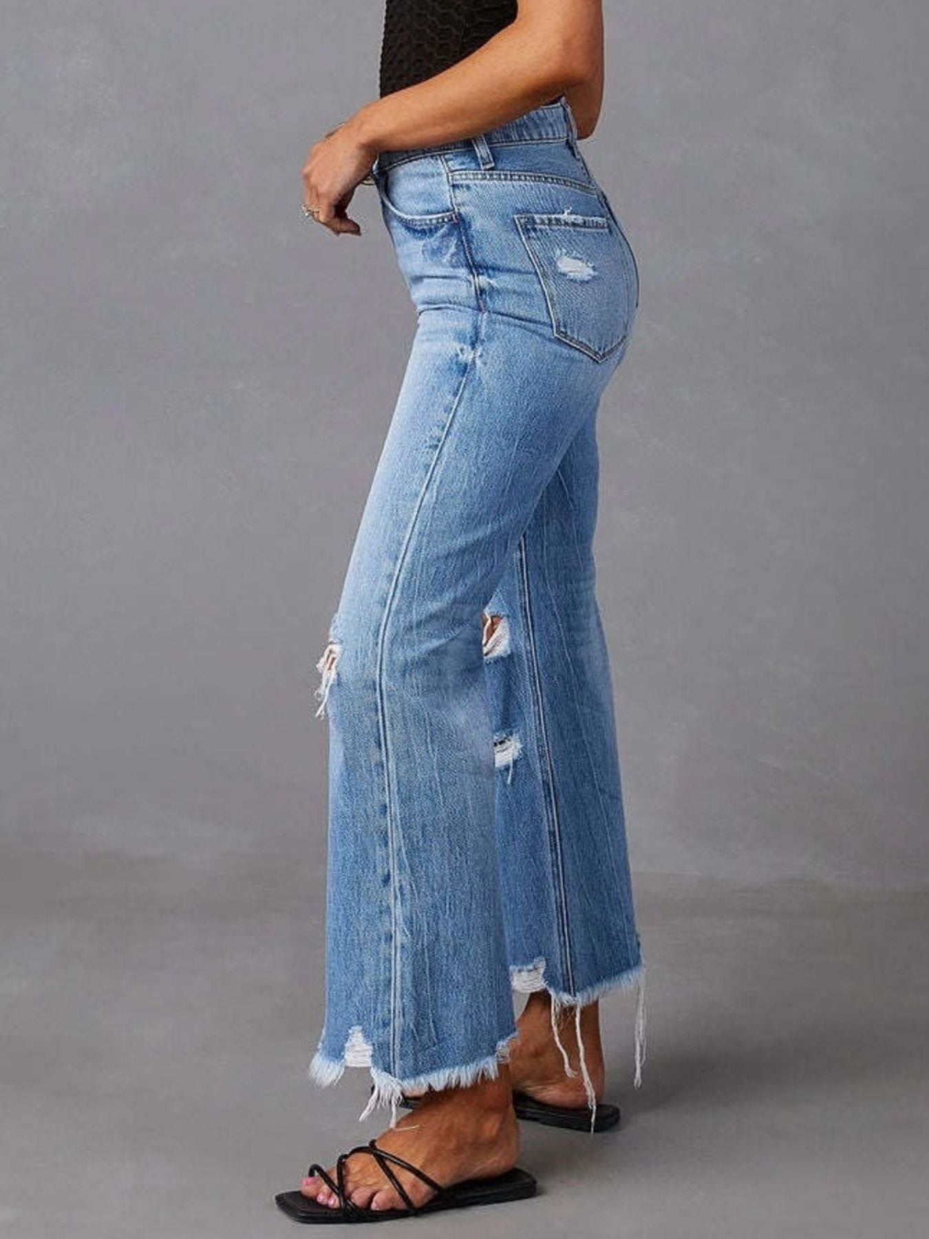 Light blue distressed flare jeans with raw hem, side rips and frayed edges, profile