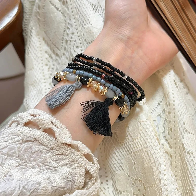Black and light blue bead tassel bracelet with gray and black tassels and gold charms