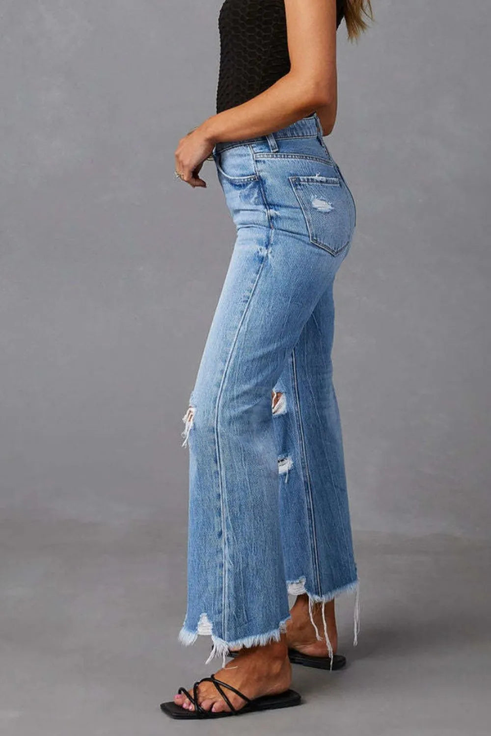 Light blue denim jeans with side distress, back pockets, and raw frayed hem