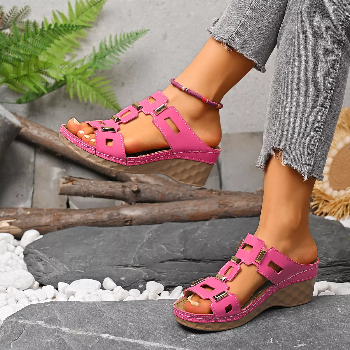 Open-toe wedge sandal in bright pink with buckle straps and open toe on stone path