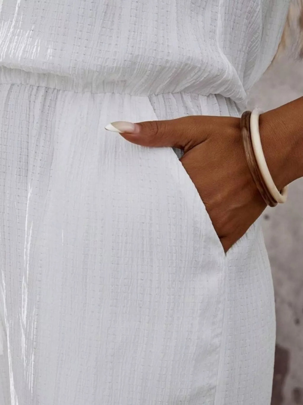 White halter jumpsuit close-up: smocked waist seam and side tie detail