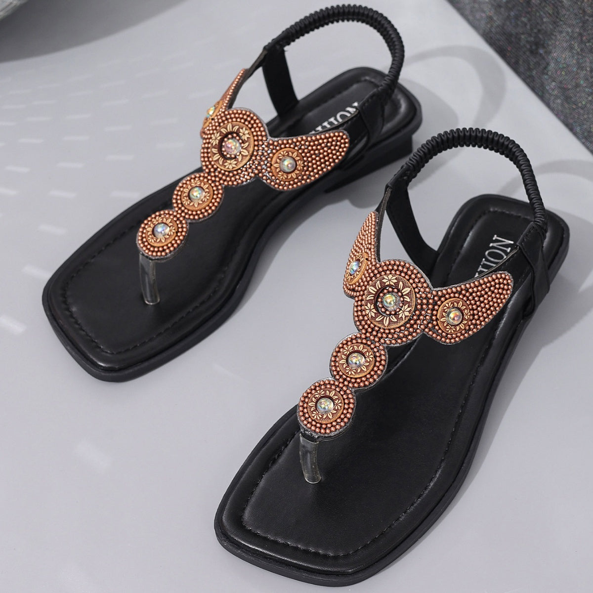 Pair of black flat thong-style T-strap sandals with bronze beaded circular accents
