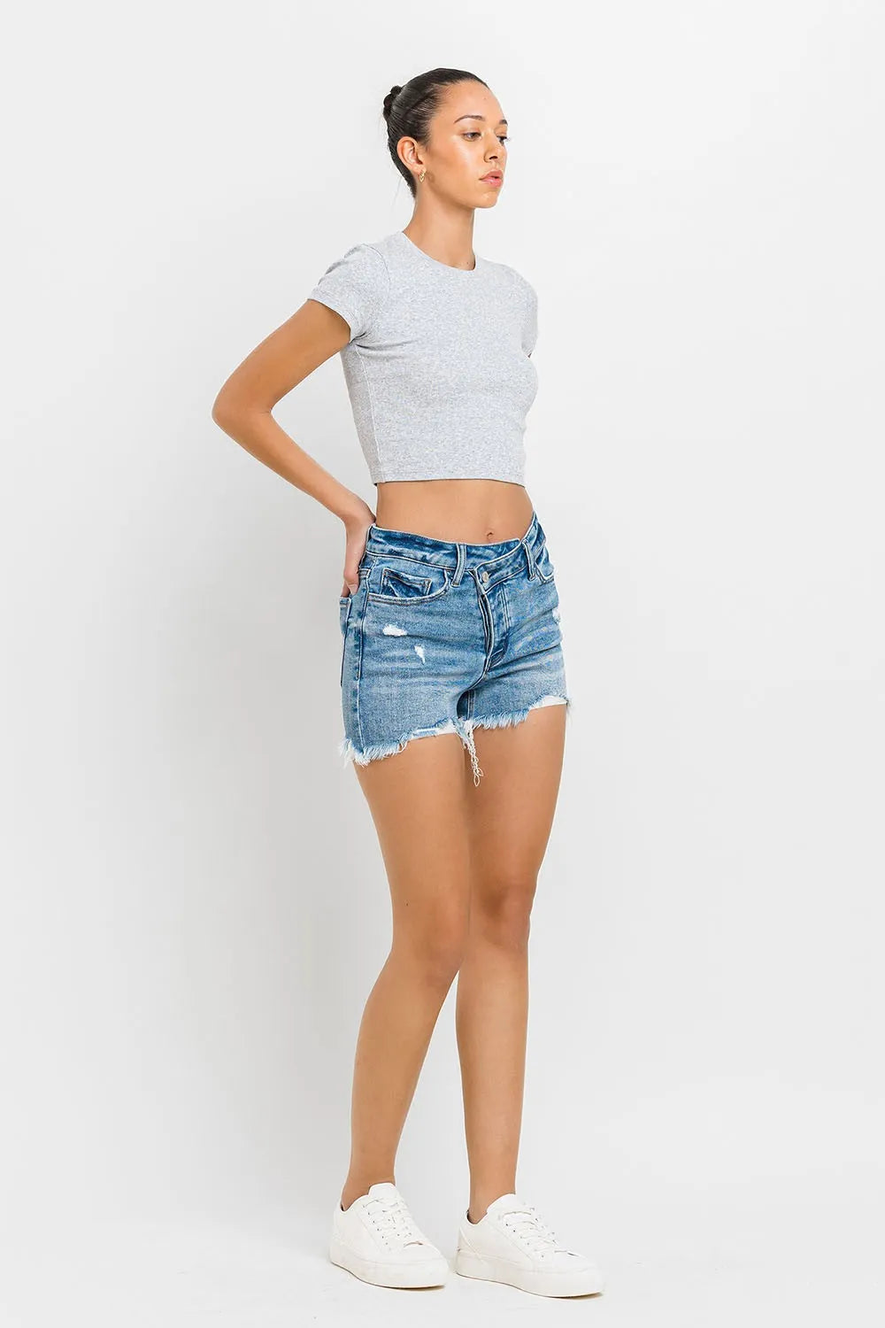 Medium-wash denim shorts, side/back view with raw frayed hem and distressing