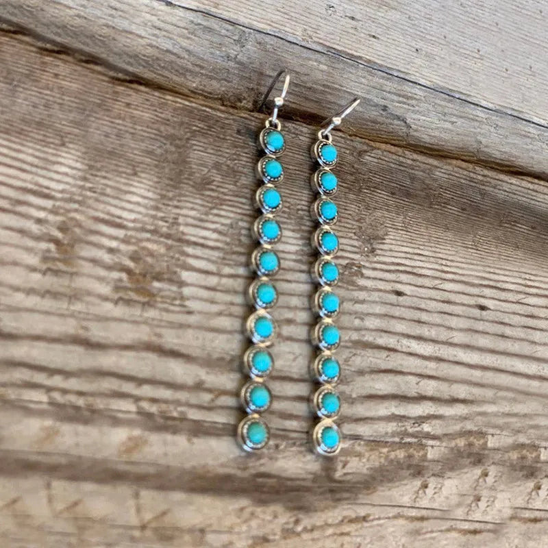 Close-up of long turquoise dangle earrings with stacked round stones and silver hooks