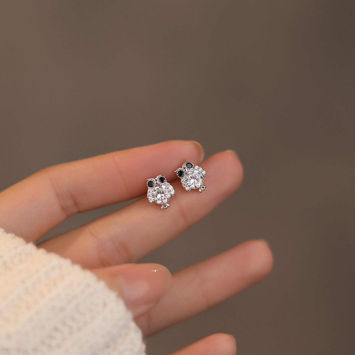 Pair of owl stud earrings held in hand, round crystal body with black eye details