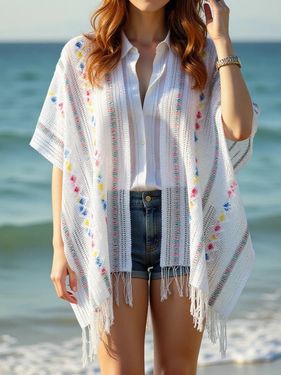 White knit cape with openwork rows, colorful dot accents, and fringe trim; open front