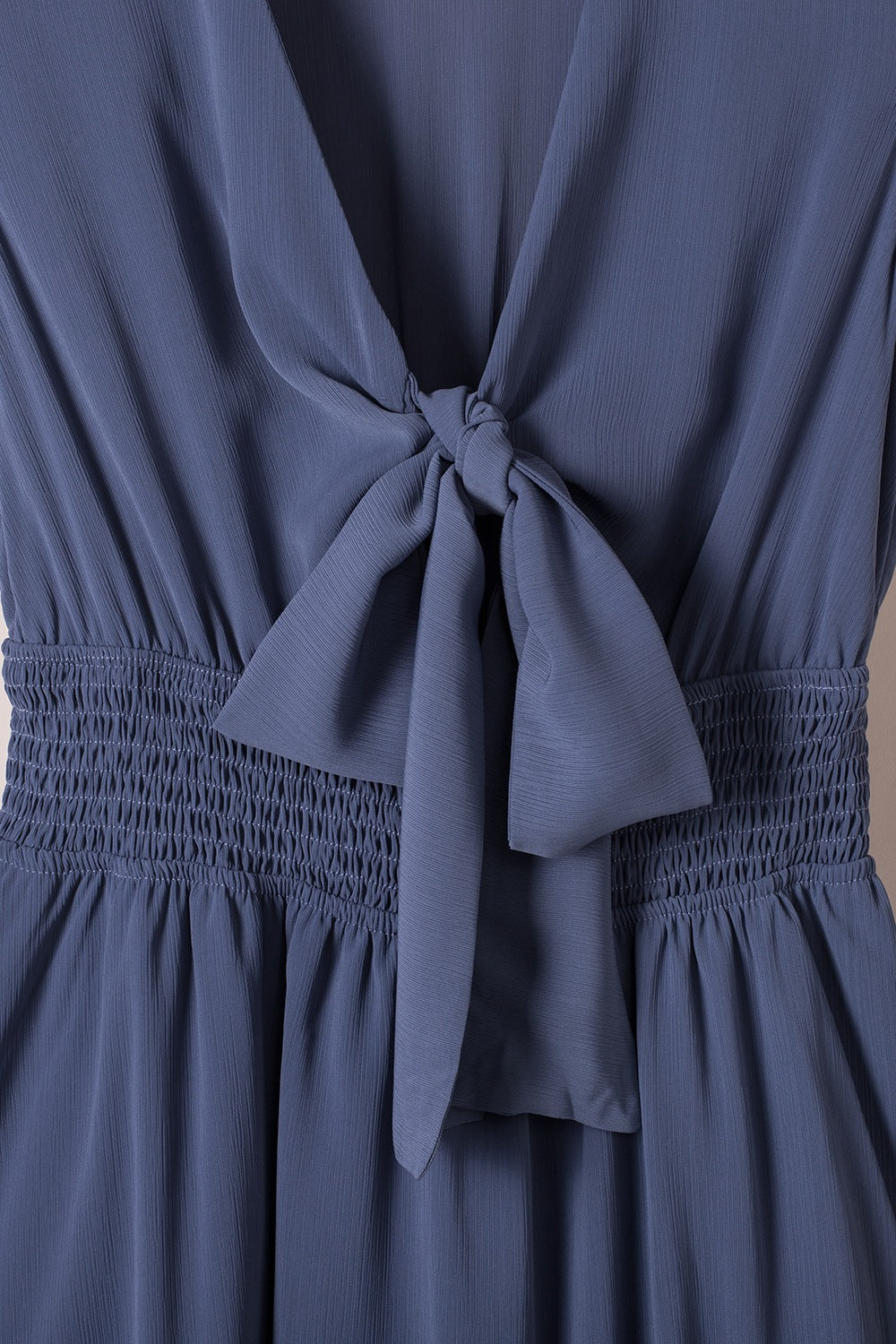 Dusty blue bow-tie V-neck mini dress close-up, gathered waist and tied front bow
