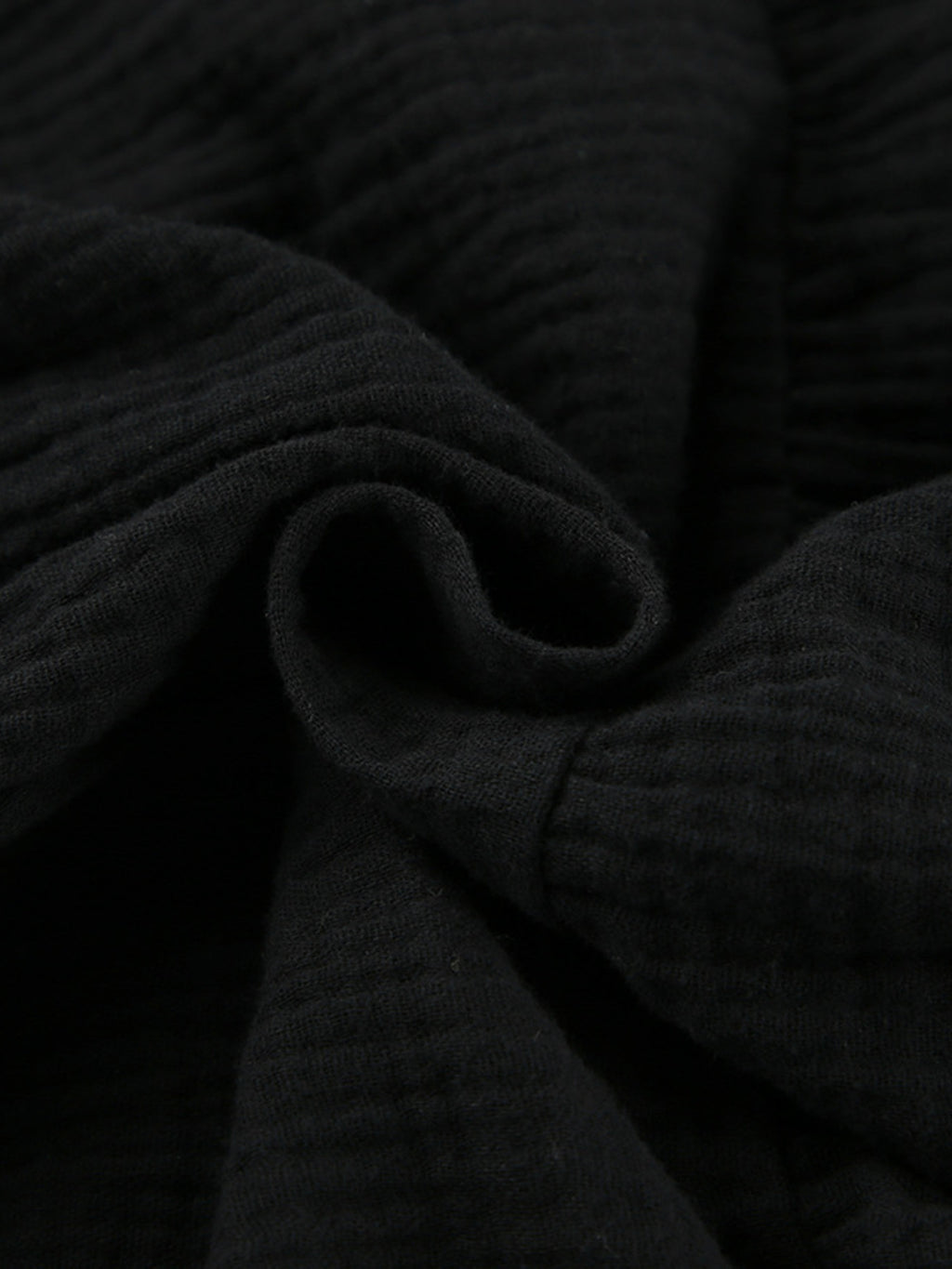 Black tiered dress fabric close-up with ribbed, ruched texture