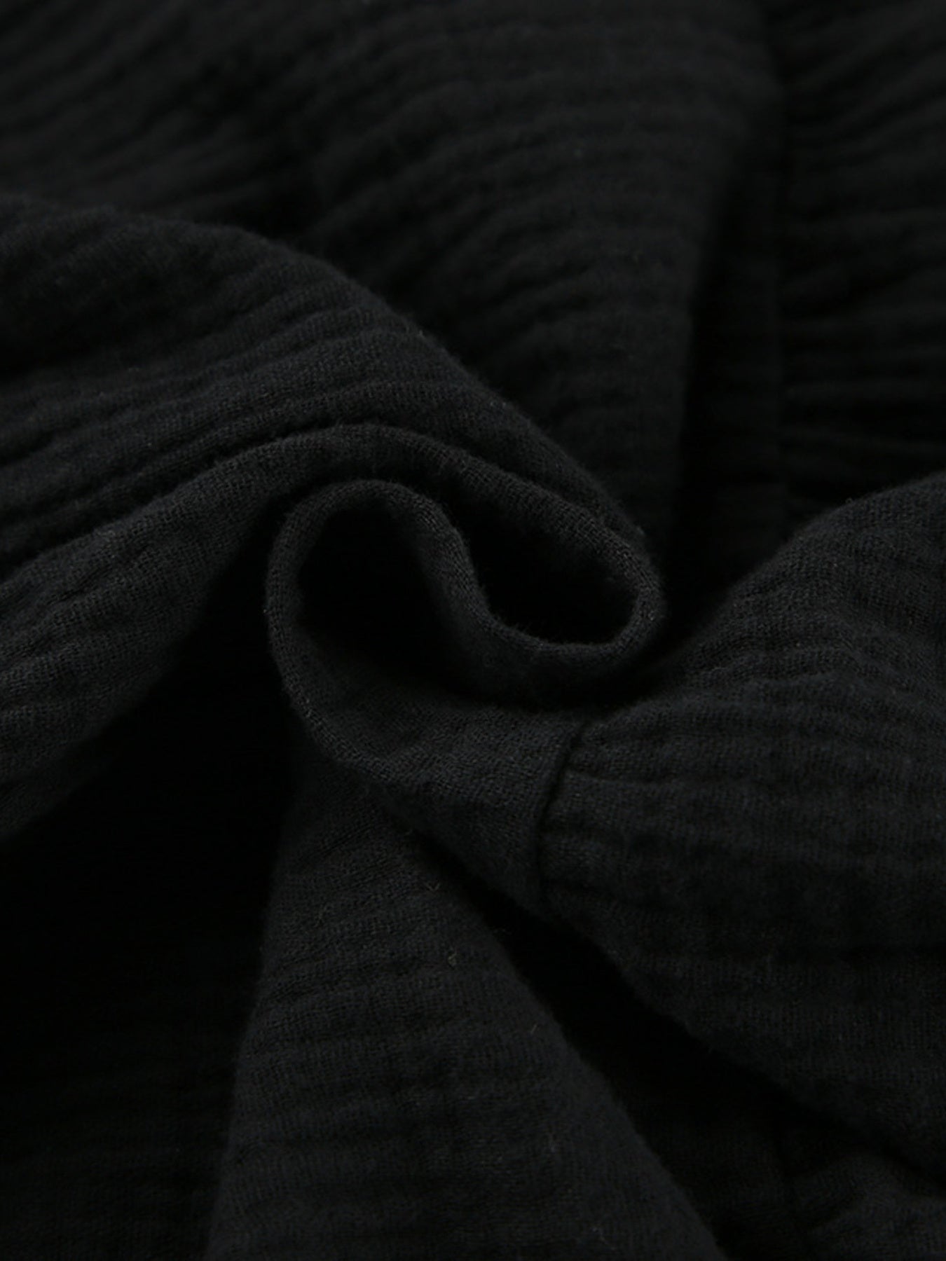 Black tiered dress fabric close-up with ribbed, ruched texture