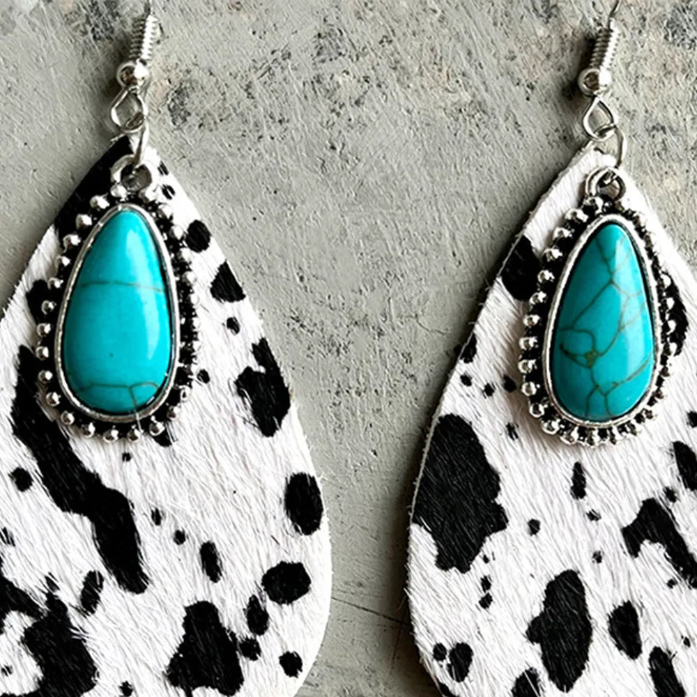 Front view of turquoise cabochon teardrop earrings on cow print leather with stud detail